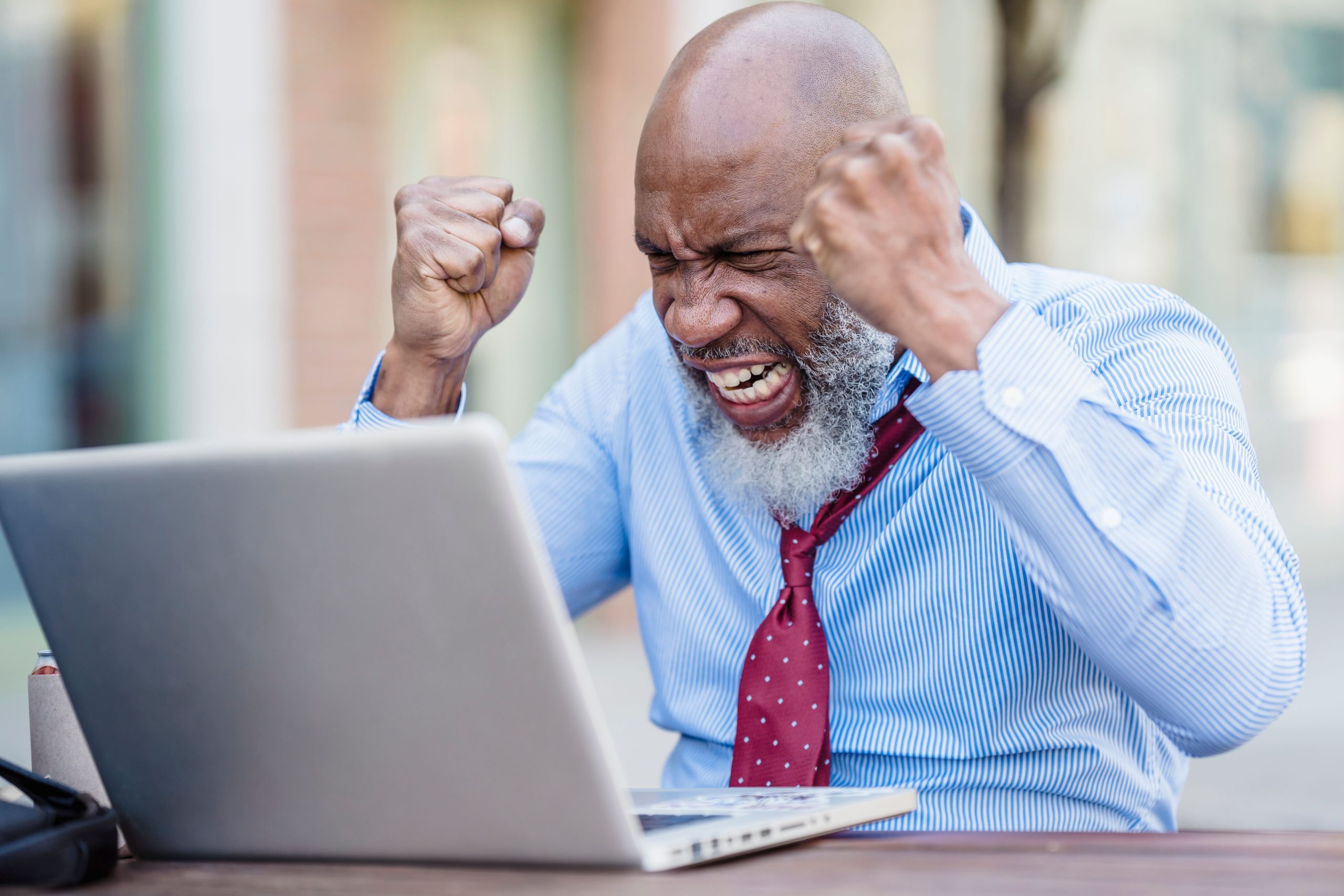 African American businessman showing frustration working on a laptop outdoors.